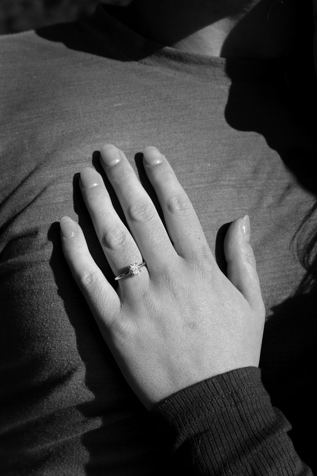 Black and white close up of a hand wearing a ring resting on a knitted sweater