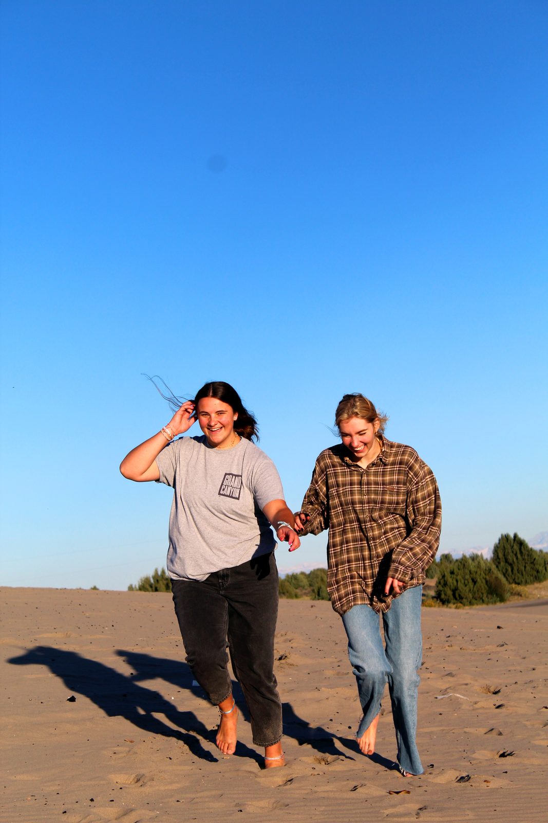 Two people walking together across sand dunes in bright sun