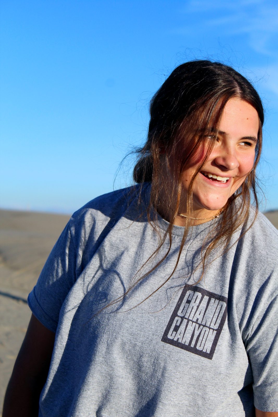 Portrait of a smiling woman in a Grand Canyon shirt against sand dunes and blue sky
