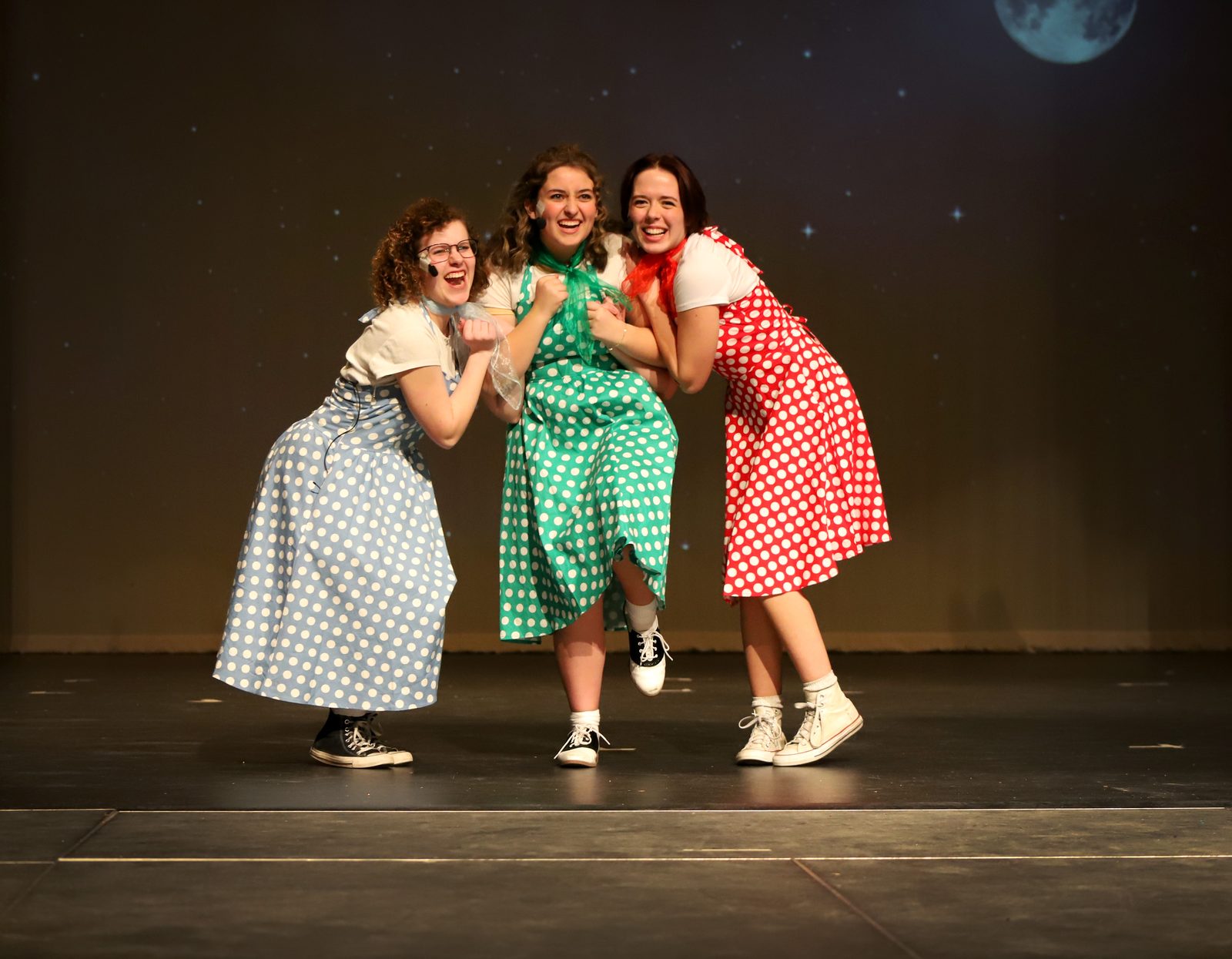 Three performers in period dresses posed together on a theatre stage