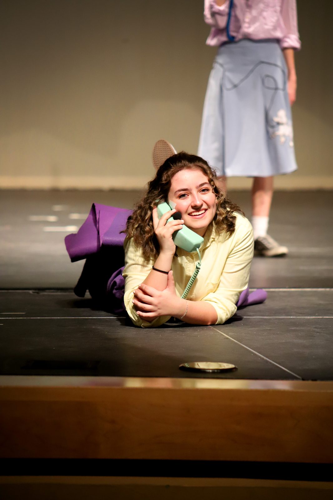 Performer lying on the stage floor holding a telephone during a scene